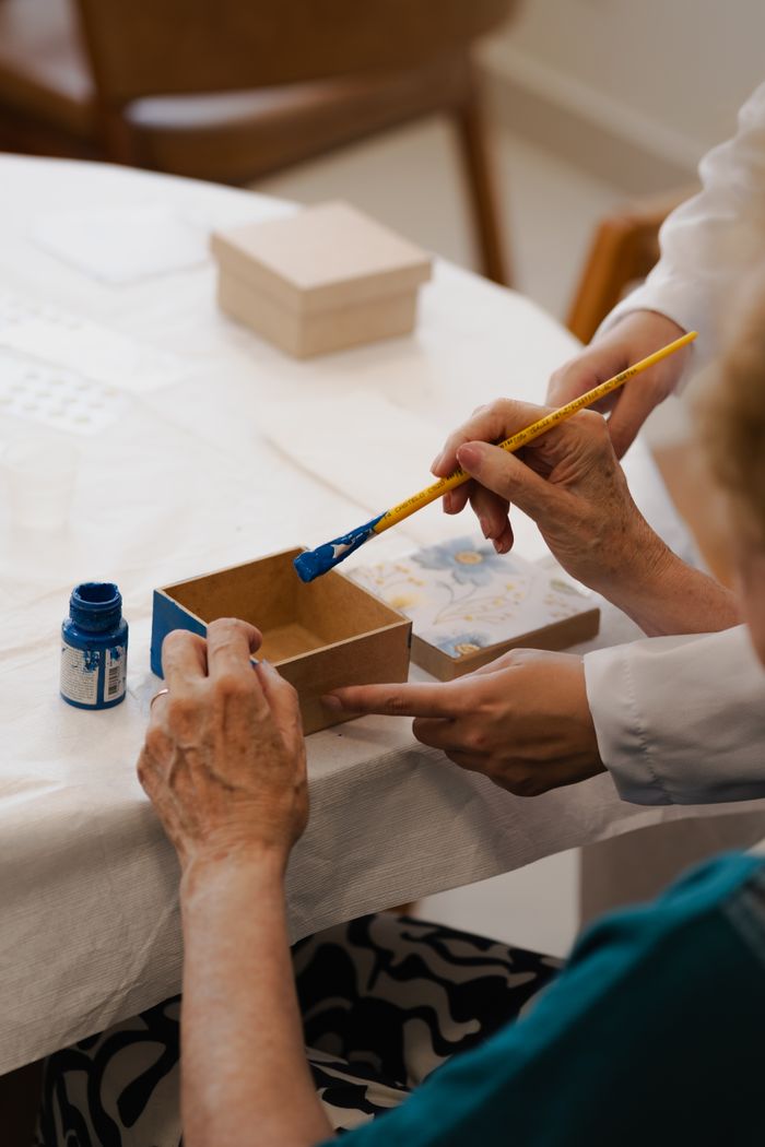 Elderly hands painting a box during a therapeutic art session, promoting relaxation and creativity.