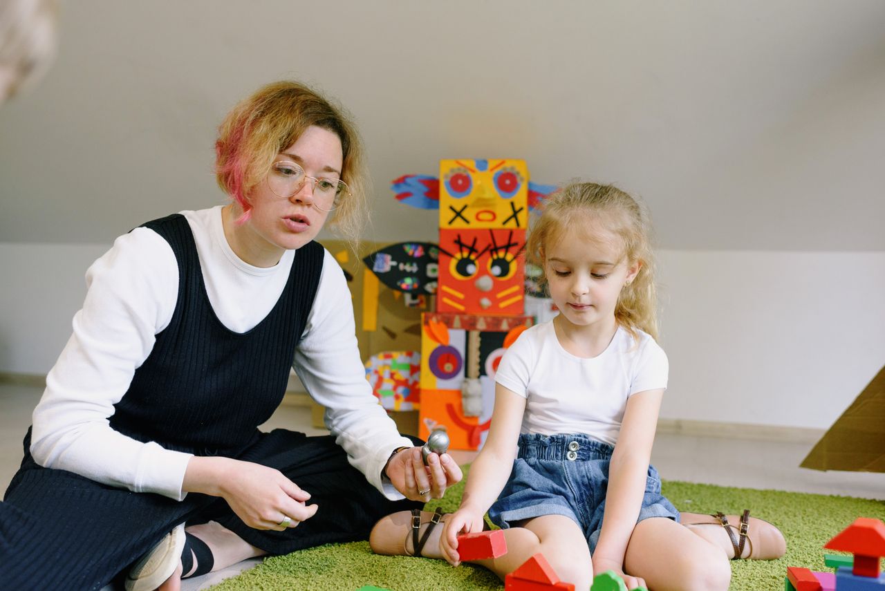 A woman and child playing with colorful wooden blocks in a playroom, creating an imaginative learning experience.